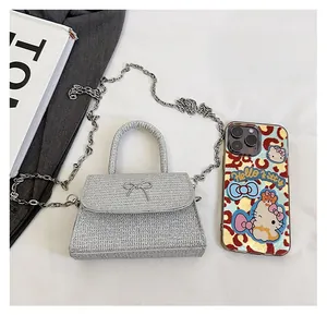 Mini trapezoid glitter crossbody bag with metallic bow detail beside a mobile phone