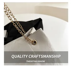 Detail view of white tote bag showing pleated texture and gold chain strap craftsmanship