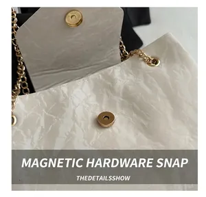 Detail of magnetic buckle closure on white pleated bag with gold chain strap