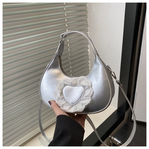 Detail of silver crescent bag featuring a metallic heart patch with white lace trim decor