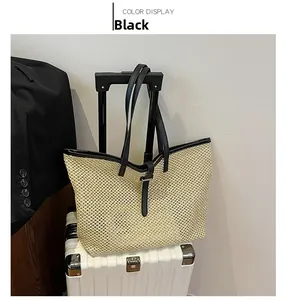 Detail of a beige straw tote bag featuring black leather trim and handle on a suitcase