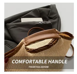 Close-up of the reinforced brown leather handle and woven texture on a beige straw tote bag