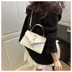 Detail of white leather crossbody bag with gold horseshoe buckle and adjustable strap