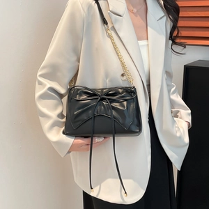 Chic black square crossbody bag with oversized bow and gold chain strap on model