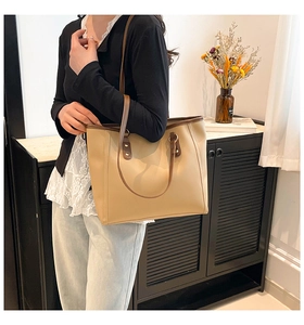 Detail of a large tote bag in beige with brown leather handles worn by a model