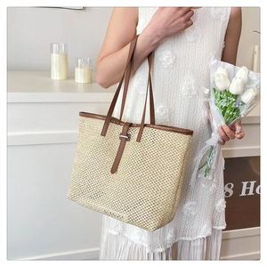 Close-up of woven straw tote bag with brown leather handles and decorative buckle detail