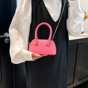 Sac coquille rose en cuir grainé avec bandoulière chaîne dorée porté par un mannequin