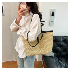 Detail of a beige woven tote bag with black leather handles held by a model in a modern room