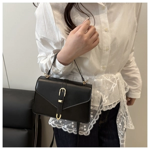 Detail of a black mini square leather handbag with gold buckle on a white shirt