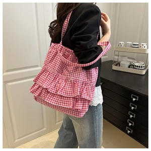 Pink and white plaid tote bag with layered ruffle details shown on a model's shoulder