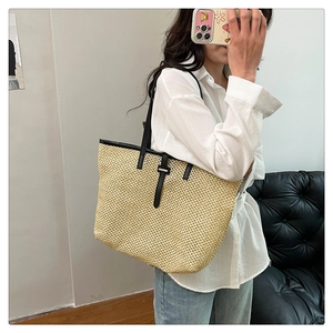 Detail view of woven straw tote bag with black leather strap and buckle closure
