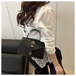 Model wearing a black leather crossbody bag with a prominent gold buckle and sleek flap design