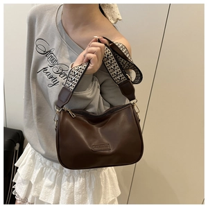 Detail of dark brown leather crescent bag with patterned strap on a casual model outfit