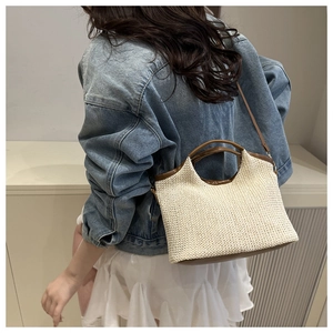 Close-up of woven straw tote bag with brown leather handles and adjustable shoulder strap