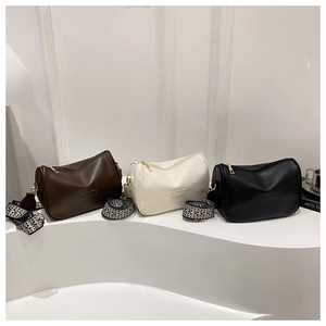 Detailed view of three minimalist cylinder bags in brown, beige, and black with wide straps