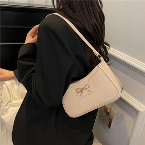 Chic beige crocodile pattern baguette bag with gold bow clasp worn by model in a room