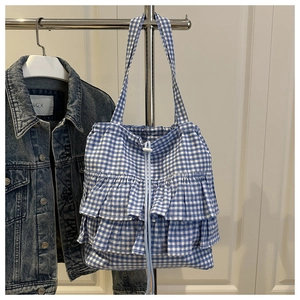 Blue gingham tote bag with triple ruffles and drawstring closure against denim backdrop