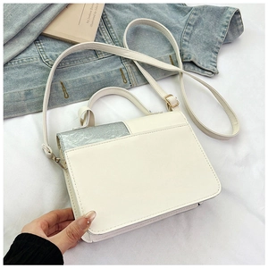 Détail d'un sac bandoulière en cuir PU blanc avec rabat argenté sur fond en denim
