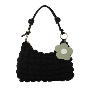 Black bubble texture shoulder bag with knotted handle and green flower charm on white background