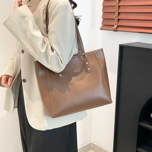 Brown leather tote bag with vertical stitching and metal rivets shown on a shoulder
