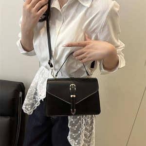 Minimalist black leather crossbody bag with gold buckle detail and top handle on model