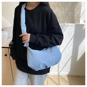 Close-up of light blue nylon dumpling bag with white Fashion label and wide strap