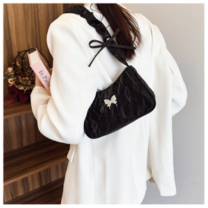Detail of black crinkle shoulder bag featuring silver butterfly buckle and ribbon bow accent