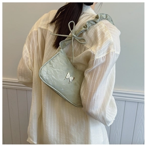 Détail du sac sous le bras vert clair avec boucle papillon argentée et bandoulière à volants