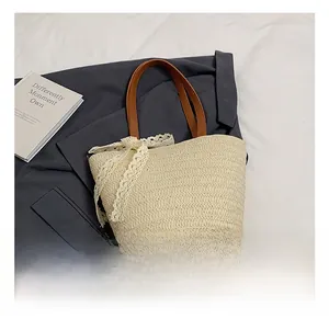 Detail of hand-woven straw tote bag featuring brown leather handles and white lace bow