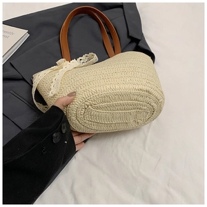 Detailed base view of bohemian straw tote bag with brown leather handles and lace bow detail