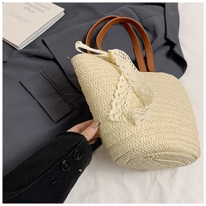 Detail of hand-woven straw tote bag with white lace bow and brown leather handle