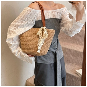 Detail of hand-woven straw tote with white lace bow and brown leather shoulder strap