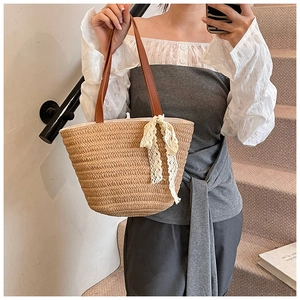 Detail of straw woven bag featuring a brown leather strap and white lace bow ornament