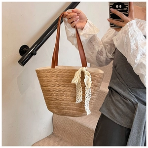 Detail of hand-woven straw tote with brown leather handles and white lace bow