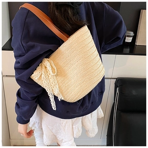 Detail of woven straw tote bag featuring a large white lace bow and leather straps