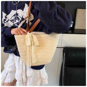 Detail of hand-woven straw tote bag featuring white lace bow and brown leather strap