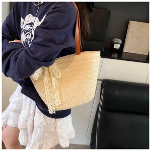 Detailed view of handmade woven straw tote with white lace bows and brown leather straps