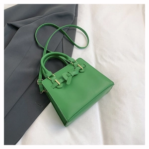 Détail du sac à main carré vert avec n'ud décoratif sur fond de blazer gris foncé