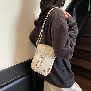 Minimalist beige nylon crossbody bag with drawstring pocket shown in lifestyle setting