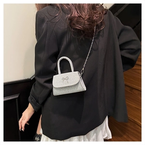 Detail of silver glitter crossbody bag with metal bow accent and chain strap worn on black suit