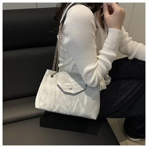 Detail of silver pleated texture shoulder bag with gold chain strap on a black sofa