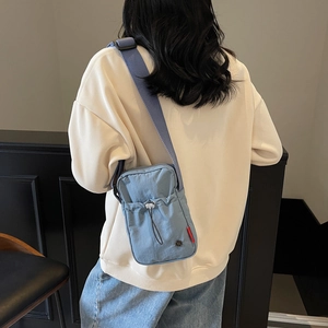 Gray-blue nylon crossbody bag with adjustable strap shown on a model in a casual setting