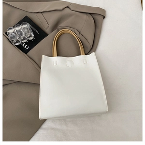 Detail of minimalist white PU leather tote bag with brown handles on textured cloth