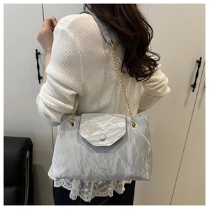 Détail du sac à chaîne plissé gris argenté avec bandoulière dorée porté à l'épaule