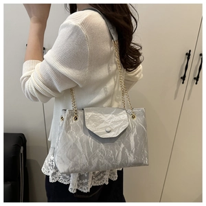 Sac à bandoulière argenté à texture froissée avec chaîne dorée sur pull blanc