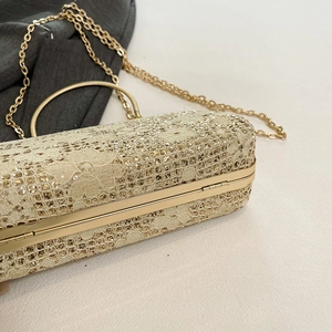 Macro shot of gold evening bag showing intricate lace patterns and shimmering sequins