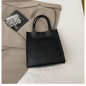 Detail view of a black minimalist rectangular handbag on a beige aesthetic background
