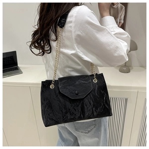 Detail of black pleated shoulder bag with gold chain strap shown on model in office