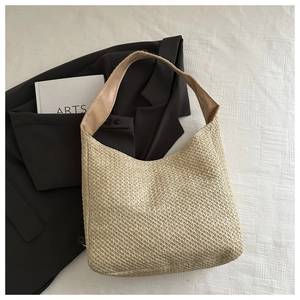 Detail of beige woven straw shoulder bag with brown leather strap on white textured cloth