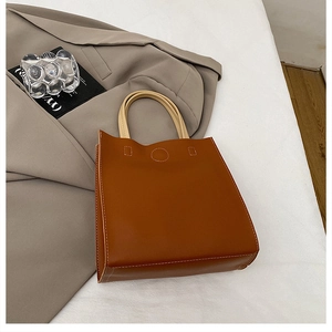 Detail of a brown leather handbag with white contrast stitching and beige top handle